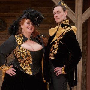 Madame Askew and the Grand Arbiter in black Victorian dress with gold brocade looking sassily at the camera