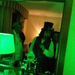 A man in a top hat looks mysteriously into a mirror bathed in green light