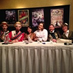 Six people in various kinds of steampunk garb sit at a long table