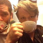 Two people face the camera, drinking from teacups