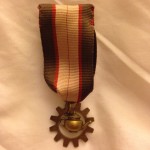 A medal with a ribbon and small metal teapot